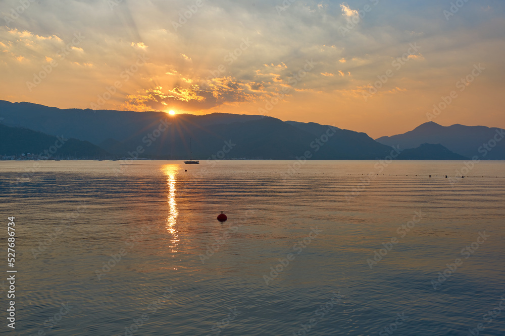 View of the rising sun over the mountains in the bay of Marmaris. Reflections of the sun in the water. The rays come out of the disk of the sun.