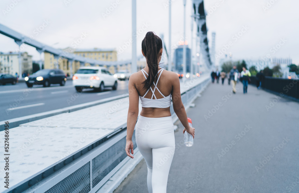 Athletic woman with water bottle walking on bridge in city