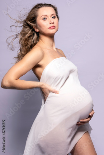 Selbstbewusste schwangere junge blonde Frau im weißen Kleid als Fotomodel für Beauty oder Glamour mit Babybauch photo