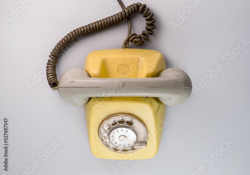 Old yellow antique rotary telephone on blue background. Vintage landline phone with dial, twisted cable and grey reciever handset. Communication, telecommunication, conversation apparatus. Top view.