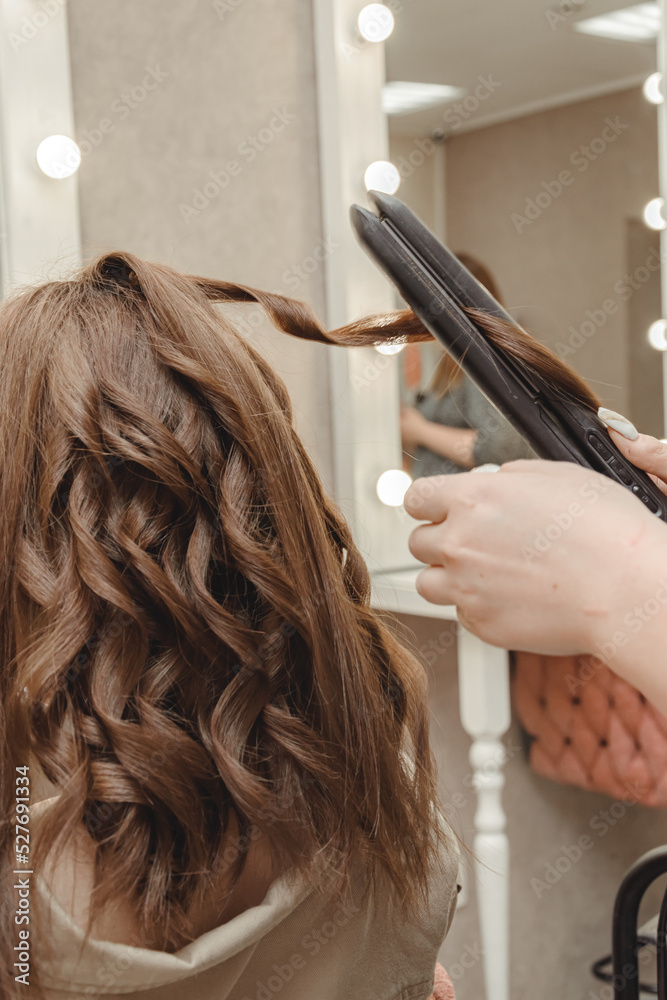 Naklejka premium girl in beauty salon is doing her hair. women's hair styling on flat iron. blog aesthetics, beauty, hair stylists. hair curling curling iron, space for text.