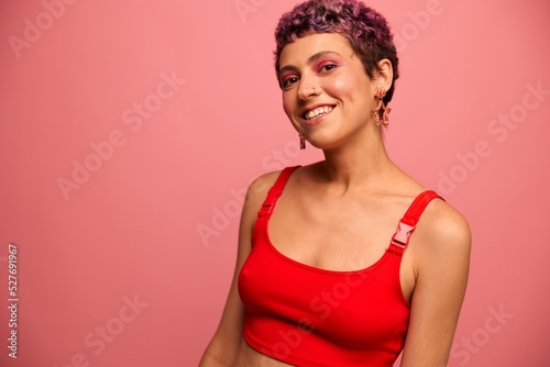 Fashion portrait of a woman with a short haircut of purple color and a smile with teeth in a red top on a pink background happiness