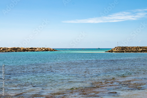 A view of a beach in Barbados with constructed rocks in the ocean. The water is blue and turquoise with rocks hidden beneath the surface.