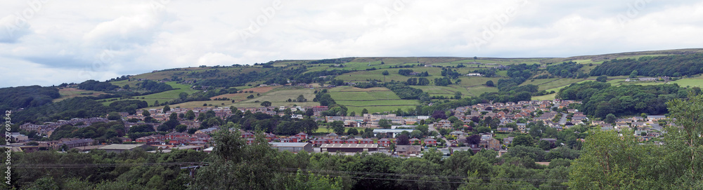 a long panoramic view of the town of mytholmroyd from above with buildings and streets of the town visible in the valley with surrounding pennine hills and fields