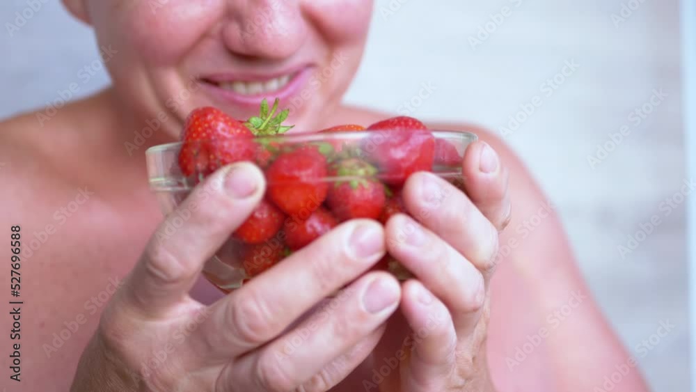 Joyful laughing Male Sniffing Smelling Strawberry with his Nose in Room. Smiling farmer holding bowl with picked berries and joking. Fruit harvest. Vitamins. Healthy food, organic seasonal food. Fun.