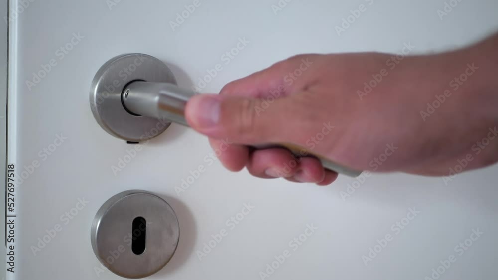 A man's hand grabs the steel handle of the white door and opens it. A man's hand grabs the steel handle of the white door and opens it.