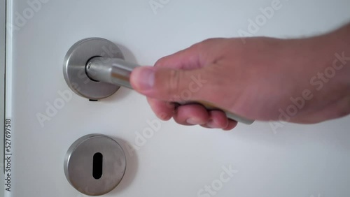 A man's hand grabs the steel handle of the white door and opens it.