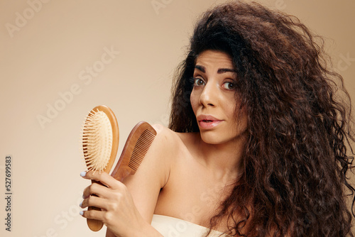 STRONG HAIR TOOLS CONCEPT. Excited happy awesome curly Latin lady hold hairbrushes open mouth say Wow posing isolated on pastel beige background, look at camera. Copy space, good banner