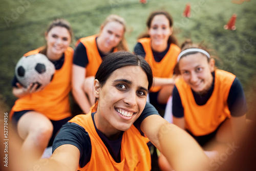 Happy female soccer team taking selfie on playing field.