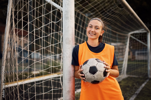 Happy female soccer player with ball on playing field looking at camera.