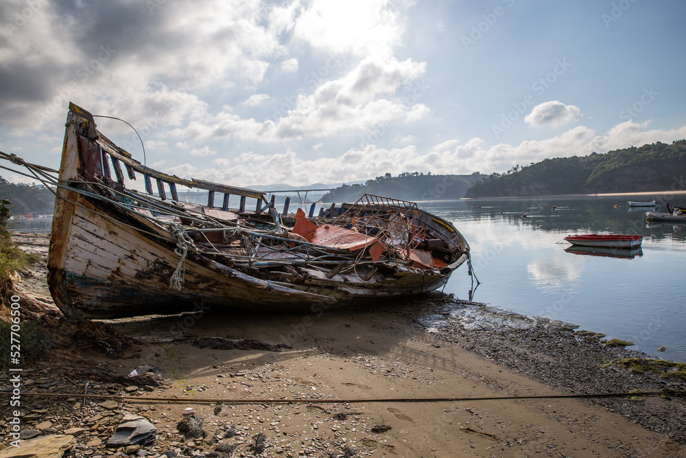a totally wrecked boat rests beside the river