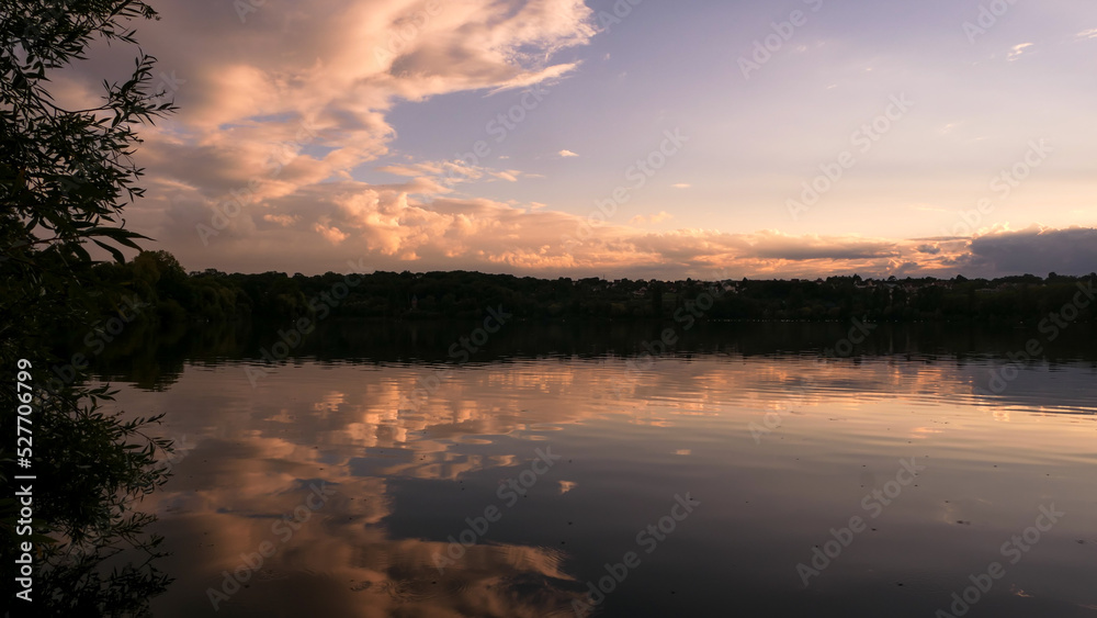 Dramatic sky over the water in rural scene. Symmetry of clouds in a lake at sunrise or sunset.
