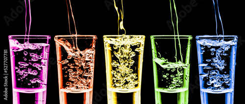 Rainbow vodka background. Five vodka shots in a row. Transparent alcohol glass background. Pouring cold vodka. Color liquor backgroud. Booze splashing into glass. Fizzy bubble party isolated on black. photo