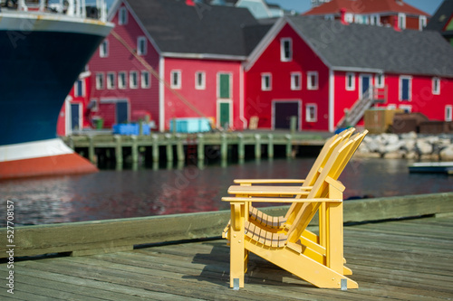 Yellow Adirondack chairs on Lunenburg pier. Colourful building and boats are visible in background photo