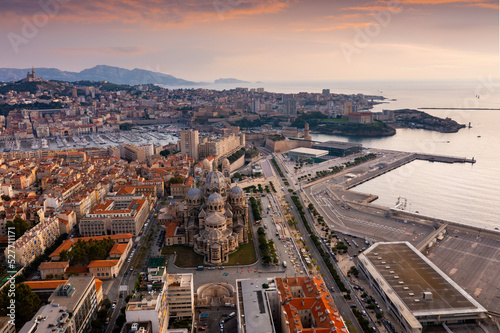 Scenic drone view of Marseille cityscape on Mediterranean coast overlooking Cathedral of Saint Mary Major, Fort Saint-Jean and Old Port with moored yachts at sunset, France