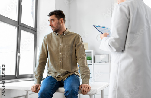 medicine  healthcare and people concept - female doctor with clipboard and male patient having health problem at hospital