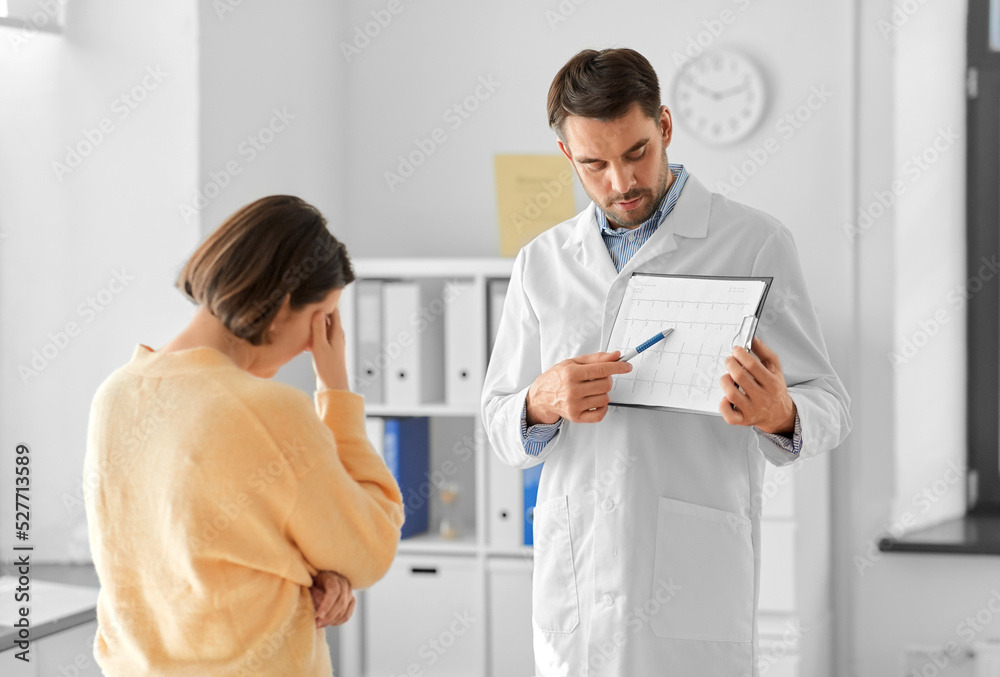 Fototapeta premium medicine, healthcare and people concept - male doctor or cardiologist with clipboard showing cardiogram to sad woman patient at hospital