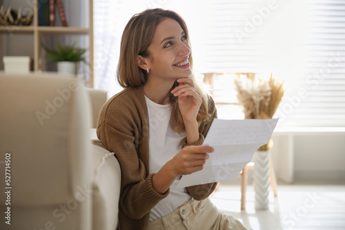 Happy woman reading letter near sofa at home photo