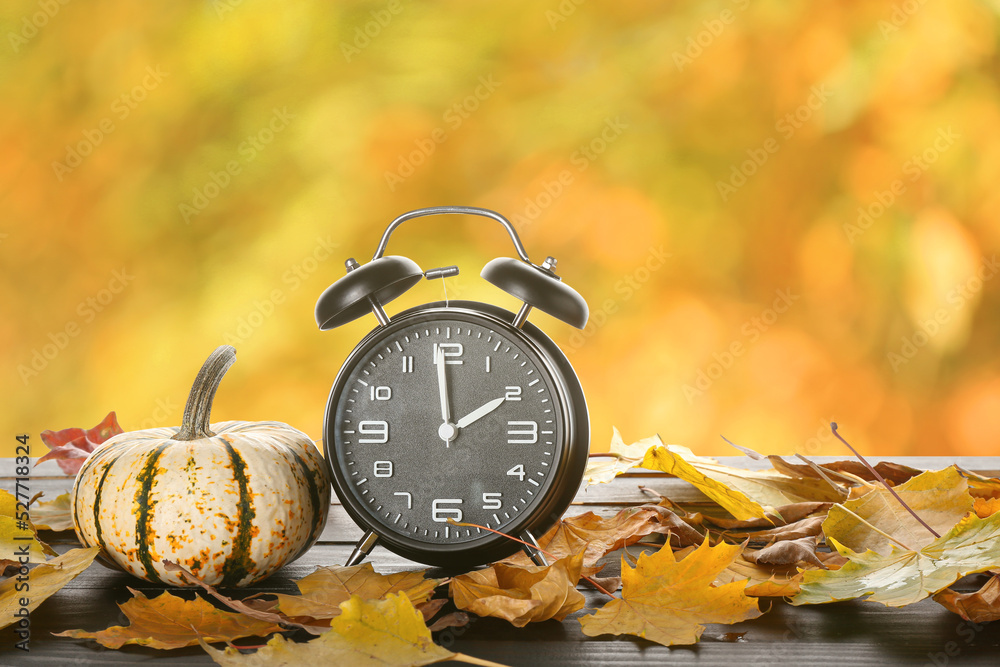 Alarm clock with autumn leaves and pumpkin on wooden table outdoors