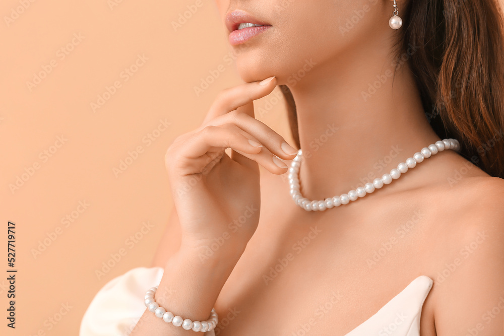 Beautiful young woman with stylish pearl jewelry on beige background, closeup