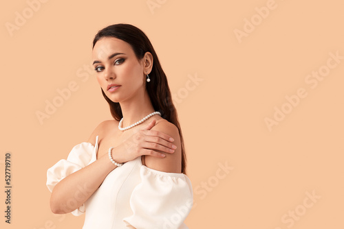 Beautiful young woman with stylish pearl jewelry on beige background Fototapet