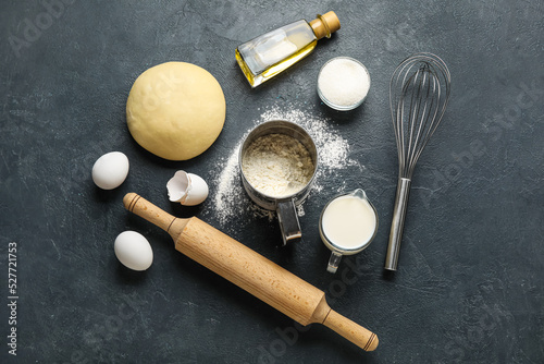 Raw dough with ingredients and utensils on dark background