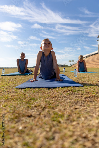 Multiracial elementary schoolboys doing upward facing dog pose exercise on yoga mat in ground