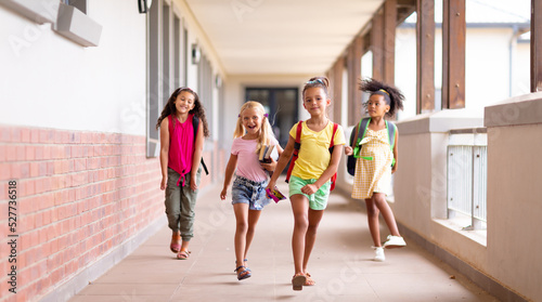 Full length of happy multiracial elementary schoolgirls walking in corridor