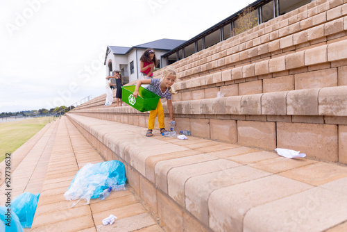 Multiracial elementary schoolgirls cleaning plastic waste on school building steps against sky