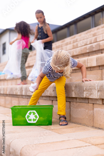 Multiracial elementary schoolgirls collecting plastic waste on school building steps