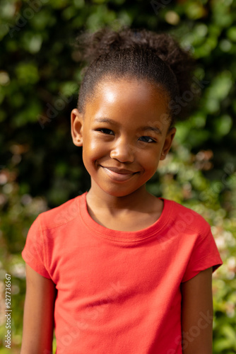 Portrait of cute smiling african american girl standing against plants outdoors