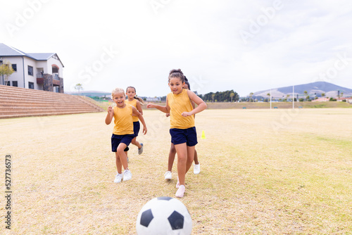 Multiracial elementary schoolgirls running towards soccer ball while playing soccer on ground