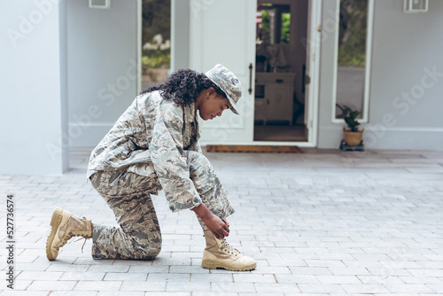 Side view of female mid adult african american soldier in uniform tying shoelace outside house