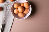 Overhead view of fresh brown eggs in bowl by wire whisk on table with copy space