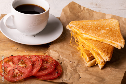 High angle view of fresh black coffee with tomato slices by cheese sandwich on wax paper