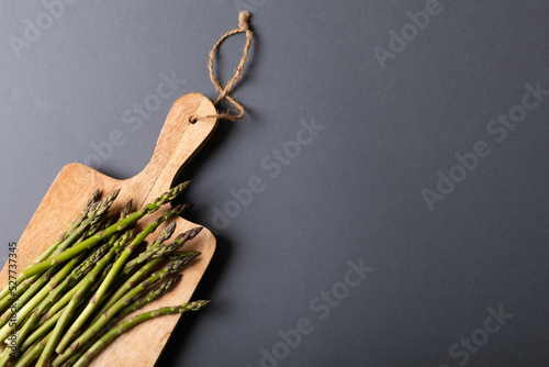Overhead view of fresh asparagus on wooden cutting board by copy space against gray background