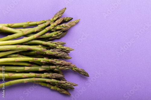 Directly above view of raw green asparagus vegetables by copy space against purple background