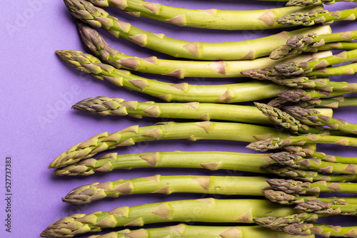 Overhead close-up view of raw green asparagus vegetables against purple background