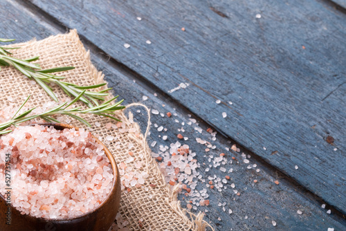 Close-up of pink rock salt in bowl by rosemary on jute fabric at table