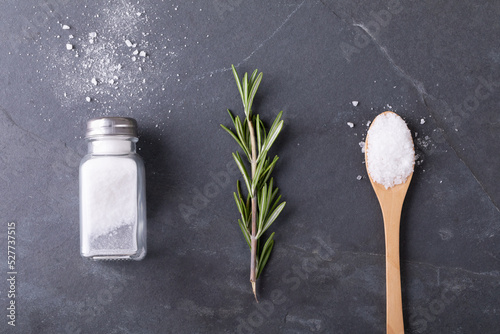 Overhead view of salt shaker with rosemary and wooden spoon arranged side by side on table
