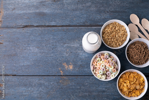 Overhead view of milk bottle with breakfast cereals in bowls by spoons on table with blank space