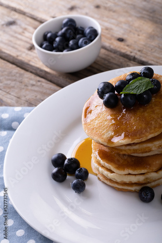 Close-up of appetizing pancakes with syrup, herb and blueberries served in plate on table