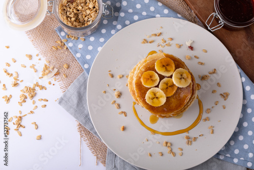 Directly above shot of pancakes with banana slices, honey and oats in plate over napkin on table