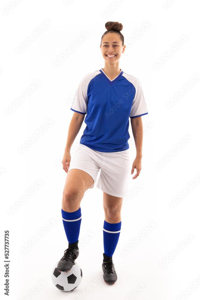 Smiling biracial young female player standing with foot on soccer ball against white background