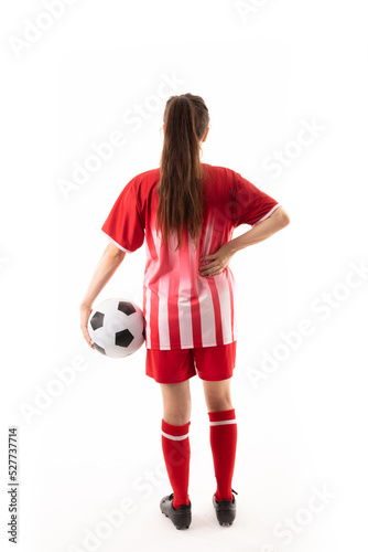 Full length of caucasian young female soccer player with ball and hand on hip over white background