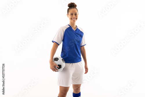 Portrait of smiling biracial young female soccer player with ball standing against white background