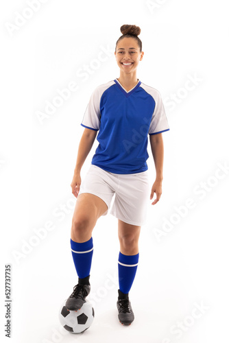 Smiling biracial young female player standing with foot on soccer ball against white background
