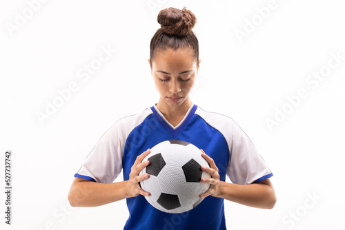 Biracial young female soccer player looking at soccer ball while standing against white background