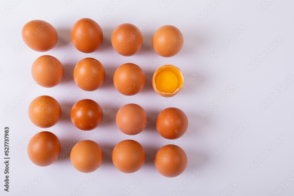 Overhead view of brown eggs with one broken egg arranged in square on table with blank space