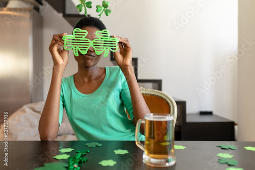 African american woman holding shamrock novelty glasses while sitting with beer mug at table